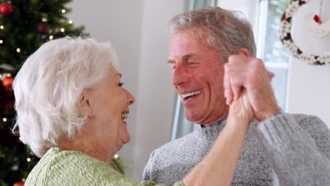Close-Up-Of-Romantic-Senior-Couple-Dancing-Together-At-Home-With-Christmas-Tree-In-Background