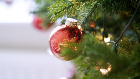Handheld,-shallow-depth-of-field-close-up-of-glittering-baubles-hanging-on-a-Christmas-tree-with-fairy-lights