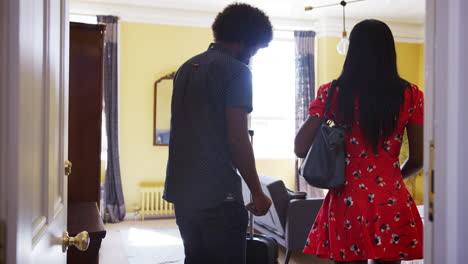 Black-couple-arrive-at-a-hotel-room-with-their-suitcases,-and-embrace-inside-the-room,-seen-from-corridor