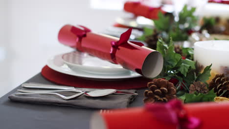 Close-up,-handheld-shot-showing-place-settings-at-a-decorated-Christmas-dining-table,-with-red-Christmas-crackers-arranged-on-plates