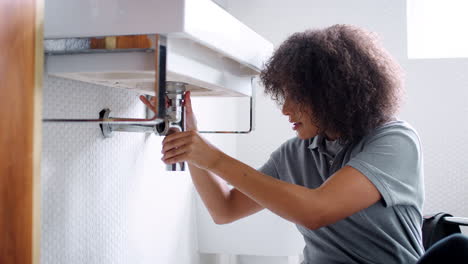 Young-black-female-plumber-sitting-on-the-floor-fixing-a-bathroom-sink-and-replacing-trap-pipe,-low-angle