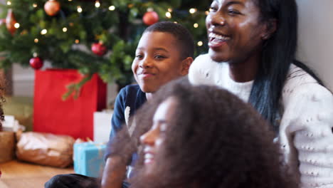 Aufgeregt-Sitzen-Die-Kinder-Mit-Ihrer-Mutter-Auf-Dem-Boden,-Während-Die-Familie-Gemeinsam-Weihnachten-Feiert