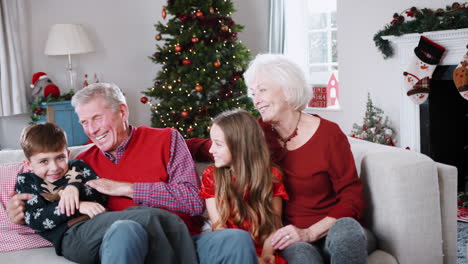 Porträt-Von-Großeltern-Mit-Enkeln,-Die-Am-Weihnachtstag-Zu-Hause-Auf-Dem-Sofa-Im-Wohnzimmer-Sitzen