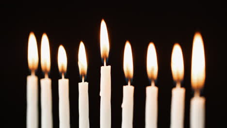 Close-up-of-nine-lit-candles-burning-for-the-Jewish-holiday-of-Hanukkah,-selective-focus