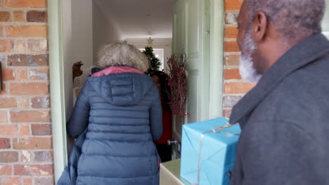 Grandparents-Being-Greeted-By-Mother-And-Daughter-As-They-Arrive-For-Visit-On-Christmas-Day-With-Gifts