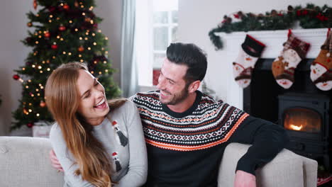 Portrait-Of-Couple-Wearing-Festive-Jumpers-Sitting-On-Sofa-In-Lounge-At-Home-On-Christmas-Day