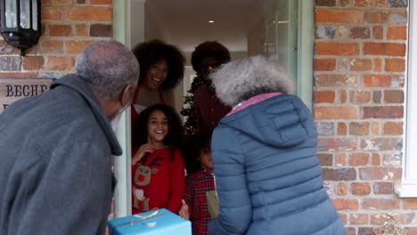 Grandparents-Being-Greeted-By-Family-As-They-Arrive-For-Visit-On-Christmas-Day-With-Gifts