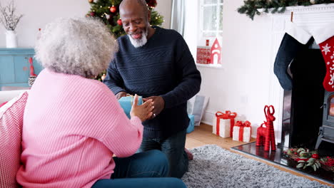 Senior-black-man-giving-a-Christmas-gift-to-his-partner,-then-they-hug-each-other,-front-view
