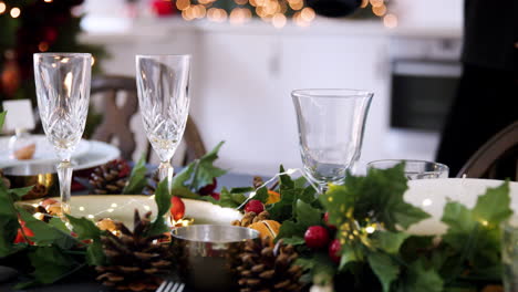 Mid-section-of-a-woman-placing-a-bottle-of-champagne-on-a-dining-table-decorated-for-Christmas-dinner,-selective-focus