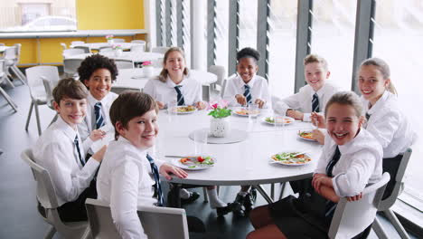 Portrait-Of-High-School-Students-Wearing-Uniform-Sitting-Around-Table-And-Eating-Lunch-In-Cafeteria
