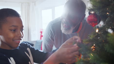 Grandfather-And-Grandson-Hanging-Decorations-On-Christmas-Tree-At-Home-Together