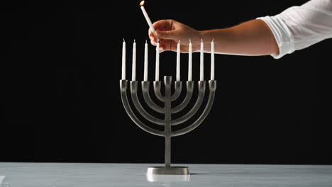 Hand-lighting-the-nine-white-candles-in-a-Jewish-menorah-sat-on-a-pale-marble-surface,-close-up,-front-view