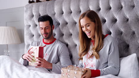 Woman-Opening-Gift-Of-Necklace-In-Bed-At-Home-As-Couple-Exchange-Presents-On-Christmas-Day