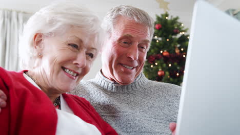 Senior-Couple-Making-Christmas-Video-Call-To-Family-On-Laptop