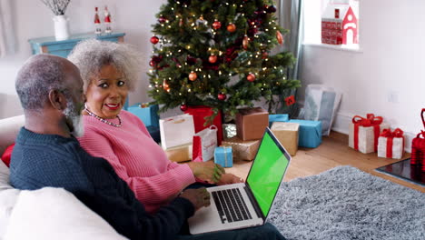 Senior-black-couple-sitting-on-the-couch-talking,-with-laptop-on-man's-knees,-Christmas-tree-and-gifts-in-background,-side-view
