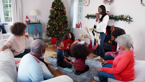 Niños-Lanzando-Papel-De-Regalo-Al-Aire-Mientras-Una-Familia-De-Varias-Generaciones-Celebra-La-Navidad-Juntos