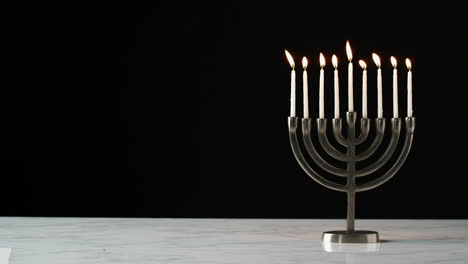 Lockdown-shot-of-candles-burning-in-a-menorah-against-a-black-background,-space-on-the-left-side-of-frame