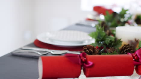 A-woman’s-hand-laying-Christmas-crackers-on-plates-at-a-table-decorated-for-Christmas-dinner,-close-up,-follow-shot