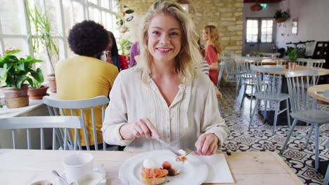 Young-adult-woman-eating-brunch,-reacting-and-talking-to-camera-at-a-restaurant,-shot-from-companion's-POV