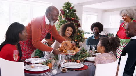 Grandfather-bringing-a-roast-turkey-to-the-dinner-table-during-a-multi-generation,-mixed-race-family-Christmas-celebration