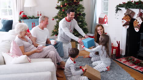 Three-Generation-Family-Wearing-Pajamas-In-Lounge-At-Home-Opening-Gifts-On-Christmas-Day
