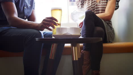 Mid-section-close-up-of-couple-in-conversation,-sitting-with-drinks-at-a-window-seat-in-a-pub,-slow-motion