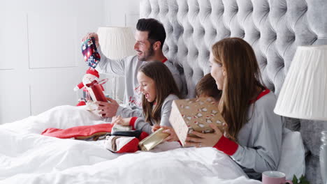 Excited-Family-In-Bed-At-Home-Together-Opening-Gifts-On-Christmas-Day