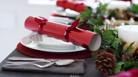 Close-up-of-decorated-Christmas-dining-table,-place-settings-with-red-Christmas-crackers-arranged-on-plates