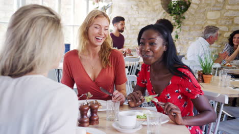 Three-young-adult-women-having-brunch-together-and-talking-in-a-small-restaurant,-waist-up