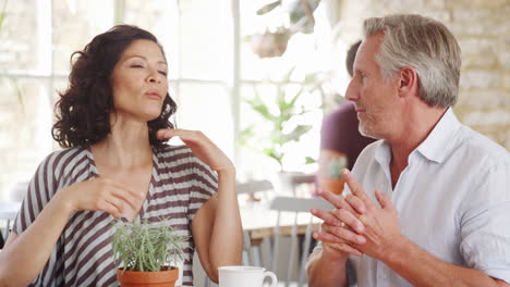 Middle-aged-woman-gesturing-while-talking-with-her-senior-white-male-friend-at-a-table-in-a-cafe,-close-up