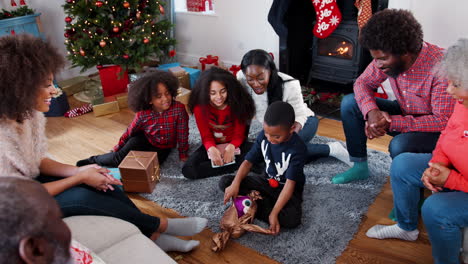 Hijo-Abriendo-Regalo-Mientras-Una-Familia-Multigeneracional-Celebra-La-Navidad-Juntos-En-Casa