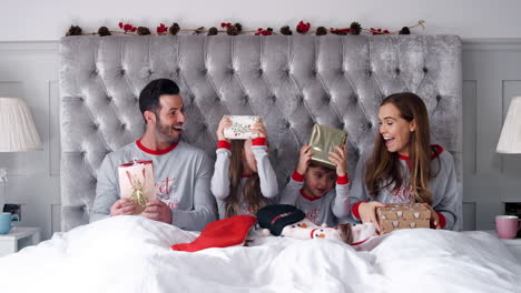 Excited-Family-In-Bed-At-Home-Together-Opening-Gifts-On-Christmas-Day