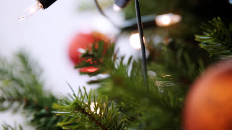 Handheld,-Geringe-Schärfentiefe-Nahaufnahme-Von-Glitzernden-Kugeln,-Die-An-Einem-Weihnachtsbaum-Mit-Lichterketten-Hängen-Hanging