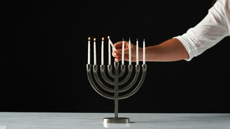 Hand-Anzünden-Der-Restlichen-Weißen-Kerzen-In-Einer-Jüdischen-Menora-Aus-Einer-Einzigen-Kerze,-Nahaufnahme,-Vorderansicht