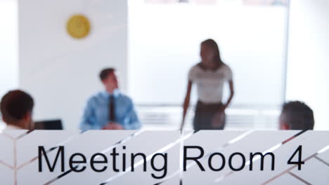 Pull-Focus-Shot-Of-Businesswoman-Giving-Boardroom-Presentation-Viewed-Through-Meeting-Room-Window-In-Slow-Motion
