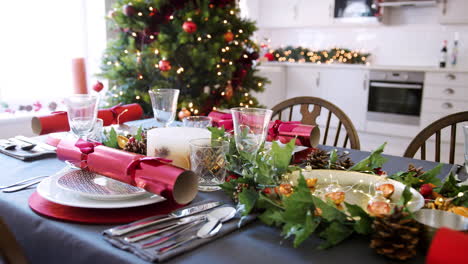 Ein-Für-Das-Weihnachtsessen-Vorbereiteter-Esstisch-Mit-Weihnachtsbaum-Und-Küchenhintergrund,-Nahaufnahme,-Die-Sich-Um-Den-Tisch-Bewegt