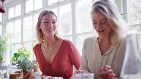 Two-young-adult-white-women-eating-lunch-with-friends-at-a-restaurant,-low-angle