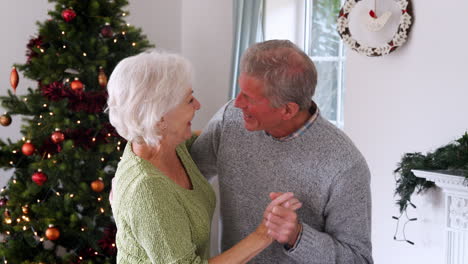 Romantic-Senior-Couple-Dancing-Together-At-Home-With-Christmas-Tree-In-Background