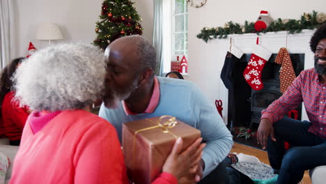 Älteres-Paar-Tauscht-Geschenke-Aus,-Während-Es-Weihnachten-Zu-Hause-Mit-Der-Familie-Feiert