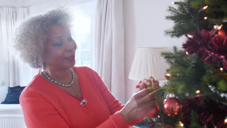 Senior-Woman-Hanging-Decorations-On-Christmas-Tree-At-Home