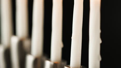 Tilt-shot-of-lit-white-candles-burning-in-a-Jewish-menorah-candelabrum,-selective-focus,-close-up-detail