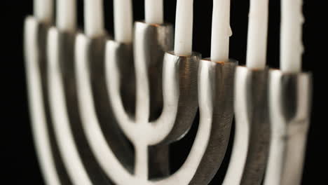 Close-up,-tight-crop-of-silver-menorah-with-white-candles-on-a-black-background,-rack-shot