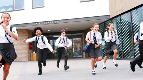 Group-Of-High-School-Students-Wearing-Uniform-Running-Out-Of-School-Buildings-Towards-Camera-At-The-End-Of-Class