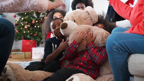 Kinder-Spielen-Mit-Einem-Riesigen-Teddybären,-Während-Eine-Familie-Mit-Mehreren-Generationen-Am-Weihnachtstag-Geschenke-öffnet