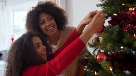 Mother-And-Daughter-Hanging-Decorations-On-Christmas-Tree-At-Home