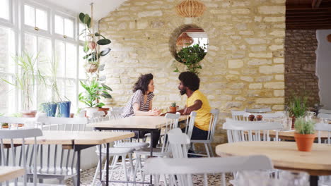 Mixed-race-middle-aged-couple-sitting-at-table-talking-in-an-empty-restaurant