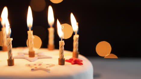 Close-up-of-lit-candles-on-a-white,-decorated-birthday-cake,-which-are-blown-out,-bokeh-lights-in-the-background