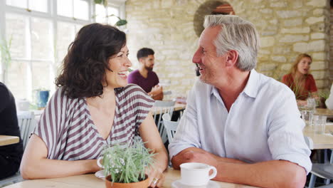 Mature-couple-laughing-and-talking-while-drinking-coffee-at-a-table-in-a-restaurant,-selective-focus