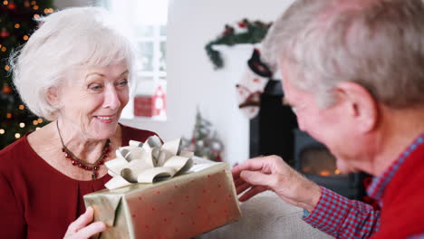 Älteres-Paar-Tauscht-Geschenke-Aus,-Während-Sie-Gemeinsam-Weihnachten-Zu-Hause-Feiern