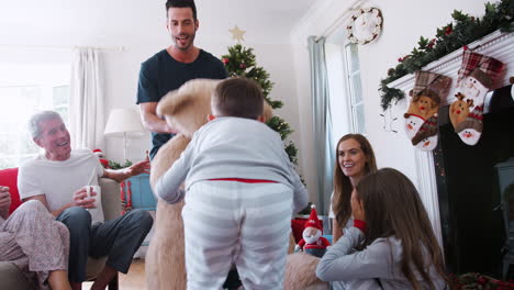Kinder-Spielen-Mit-Einem-Riesigen-Teddybären,-Während-Eine-Familie-Mit-Mehreren-Generationen-Am-Weihnachtstag-Geschenke-öffnet